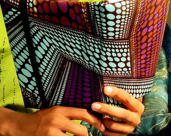 May include: A person is reading a book with a colorful patterned cover. The cover features a geometric design with brown, purple, blue, and white circles.