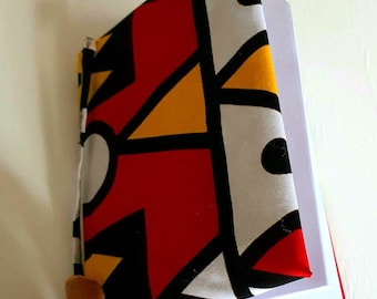 May include: A notebook with a colorful geometric pattern cover. The cover is made of fabric and features red, yellow, black, and white colors. The notebook is open to reveal blank pages.