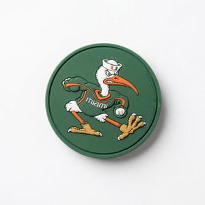 May include: A green circular coaster featuring the University of Miami mascot, a running ibis. The ibis is depicted in orange, white, and green, wearing a sailor hat and a jersey with the word "Miami".