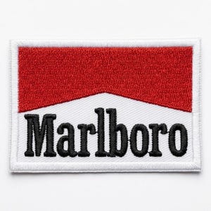 Puede incluir: Parche bordado con el logotipo de Marlboro. El parche tiene un borde blanco, una sección superior roja y la palabra "Marlboro" en letras negras y en negrita. El parche es de forma rectangular.