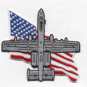 May include: Embroidered patch featuring a gray A-10 Thunderbolt II aircraft design, superimposed over a stylized American flag. The patch has a detailed, textured appearance, with the stars and stripes of the flag clearly visible. The aircraft is depicted in a top-down view.