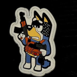 Puede incluir: Un parche de dibujos animados que representa a un personaje de perro azul sosteniendo un rifle y una pistola. El perro lleva un mono azul, un chaleco táctico naranja y botas blancas. El parche tiene un borde blanco, sobre un fondo negro.
