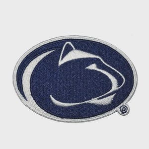 May include: A navy blue and white embroidered patch featuring the Penn State Nittany Lion logo. The oval-shaped patch has a white border and a small, circular logo on the lower right.