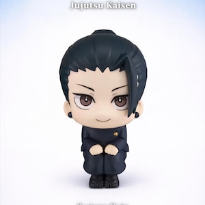 May include: A Jujutsu Kaisen Suguru Geto figure. The figure is wearing a dark blue uniform and has black hair. The figure has a cute, chibi-style design. The text "Jujutsu Kaisen" and "Suguru Geto" are visible.