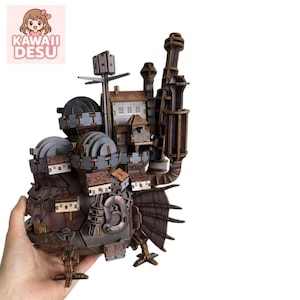 May include: A complex, multi-tiered wooden model of a mechanical castle featuring various interconnected structures, circular turrets, and a large fan-like appendage. The structure is composed of dark brown and grey wood pieces with small white accents.
