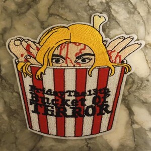 Op de afbeelding: Geborduurde patch met een vrouwengezicht en handen die uit een rood-wit gestreepte emmer komen. De tekst "Friday The 13th Bucket Of Terror" staat op de emmer. De patch heeft een witte rand.