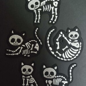 Könnte beinhalten: Fünf schwarze Katzen-Skelett-Patches mit weißen Stickdetails. Die Patches zeigen verschiedene Katzenposen, darunter stehend, sitzend und zusammengerollt. Diese Patches sind ideal für Halloween- oder Gothic-Themen-Bastelarbeiten.