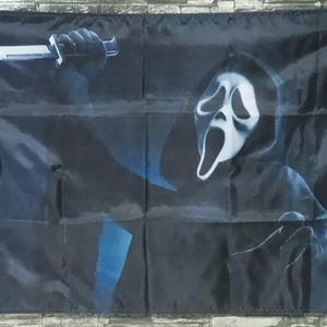 Könnte beinhalten: Schwarze Flagge mit einer Scream-Maske und einer Hand, die ein Messer hält. Die Maske ist weiß mit schwarzen Akzenten, und das Messer hat eine silberne Klinge. Der Hintergrund ist dunkel, mit blauen Akzenten.