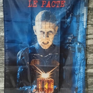 May include: A dark blue banner with the words "HELLRAISER" and "LE PACTE" in red. The image shows a character with pins in their head, holding a glowing puzzle box. The background is dark blue with chains, creating a horror theme.