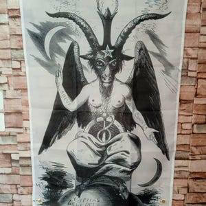Pode incluir: Uma bandeira branca com uma ilustração detalhada em preto e branco de Baphomet, uma divindade com cabeça de bode. A imagem inclui um pentagrama, luas crescentes e texto nos braços. A bandeira tem ilhós de latão para pendurar.
