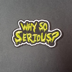 May include: An embroidered patch featuring the text WHY SO SERIOUS? in a bright lime green, dripping font style. The lettering is set against a black background with a thick white border that follows the irregular, organic shape of the text.