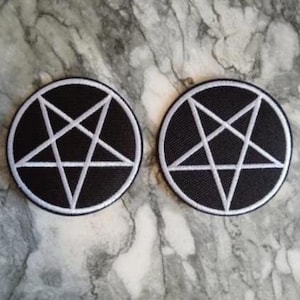 Peut inclure: Deux écussons circulaires noirs avec un pentagramme blanc. Le pentagramme est bordé de blanc, et les écussons ont une bordure blanche. Ces écussons sont probablement pour les vêtements ou les accessoires.