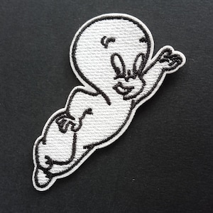 May include: A white embroidered patch featuring a cartoon ghost character with black thread outlines. The ghost is depicted in a floating pose with one arm extended upward, large oval eyes, and a small smiling mouth, rendered in a textured stitch.