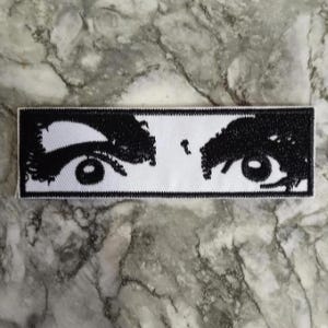 Peut inclure: Un écusson rectangulaire avec une illustration en noir et blanc d'une paire d'yeux. Les yeux sont dessinés avec des lignes noires épaisses sur un fond blanc. Ce patch est destiné à être appliqué sur des vêtements ou des accessoires.
