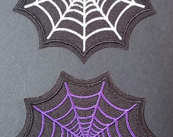 Könnte beinhalten: Zwei gestickte Aufnäher in Form von Spinnennetzen. Ein Aufnäher zeigt ein weißes Netzdesign auf schwarzem Grund, während der andere ein violettes Netzdesign auf schwarzem Grund aufweist. Beide Aufnäher haben einen markanten, gezackten Rand.