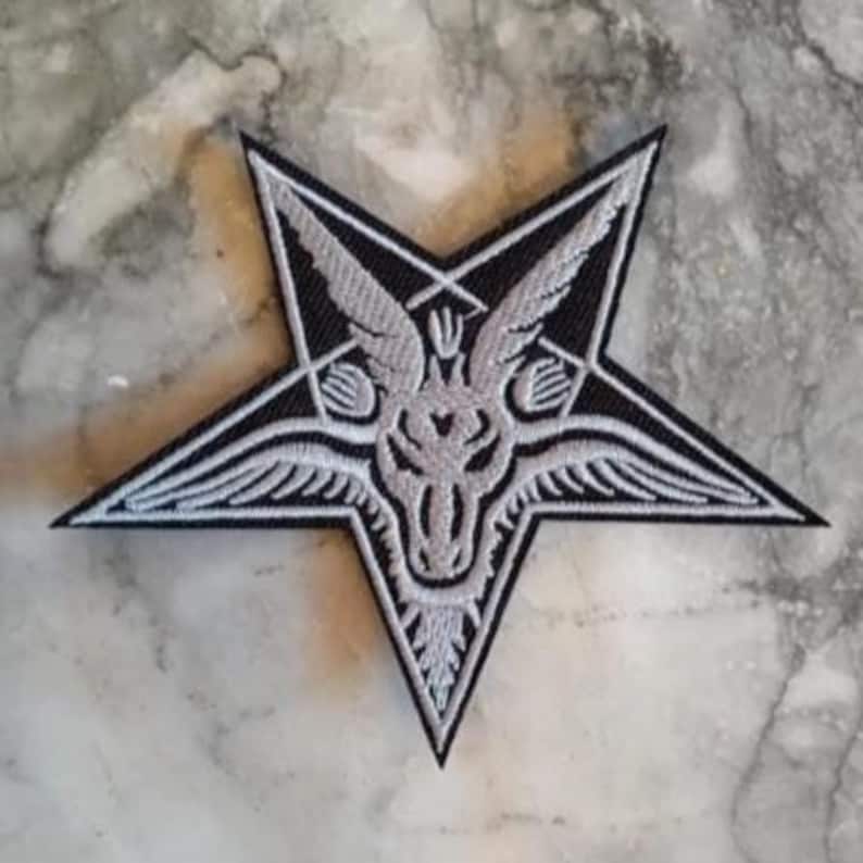 Op de afbeelding: Een zwart-wit geborduurde patch in de vorm van een vijfpuntige ster. De patch toont een gedetailleerd beeld van een geitachtig figuur met vleugels en een pentagramsymbool. Het ontwerp is ingewikkeld en de kleuren zijn opvallend.