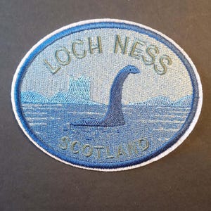 Peut inclure: Écusson brodé ovale représentant le monstre du Loch Ness dans des tons bleus. Le patch comprend les mots "LOCH NESS" et "SCOTLAND" en vert clair, avec une bordure blanche.