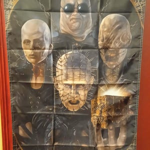 Peut inclure: Bannière noire Hellraiser avec plusieurs personnages du film d'horreur. La bannière comprend le texte "HELLRAISER" et le slogan "He'll tear your soul apart."