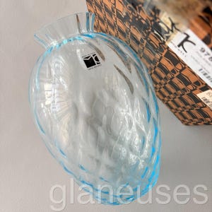 May include: A clear, light blue glass vase with a textured, patterned surface. The vase has a wide, rounded body and a flared, ruffled rim. The base of the vase is also light blue. The label says "Made in Italy".