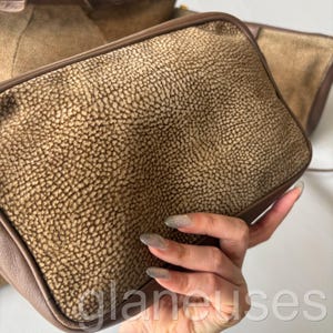May include: A set of brown leather bags with a textured surface. The bags have a rectangular shape with rounded corners and a darker brown trim. The bags are held in a person's hand.