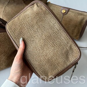 May include: A collection of brown leather handbags with a textured surface. The bags have a rectangular shape with rounded corners and brown trim. One bag is held by a hand. The bags are in various sizes and styles.