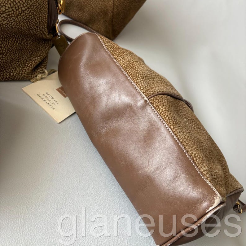 May include: Brown leather handbag with a textured, spotted pattern on the sides and a smooth, solid brown leather body. The bag has a handle and a tag that reads "Redwall Quality Guarantee".