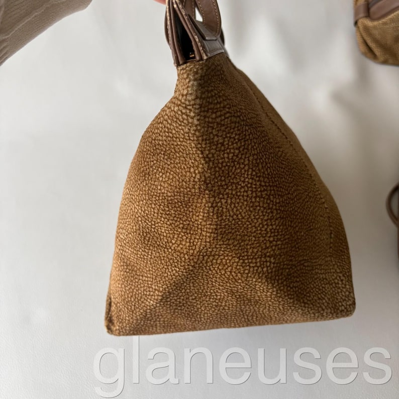 May include: A brown textured handbag with a leather handle. The bag has a triangular shape and a pebbled surface. The handle is a darker shade of brown. The word "glaneuses" is visible at the bottom of the image.