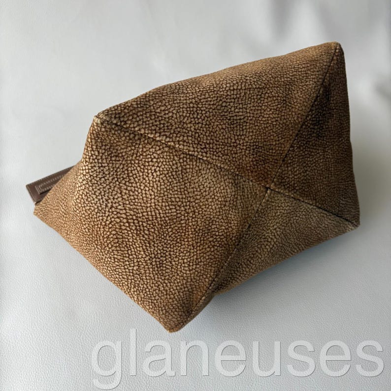 May include: A brown textured handbag with a rectangular shape. The bag has a leather handle and a textured surface. The bag is made of a durable material and is suitable for everyday use.