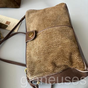 May include: A brown leather shoulder bag with a textured surface and a flap closure. The bag features a gold-colored clasp and a long, thin shoulder strap. The bag has a rectangular shape and a small front pocket.