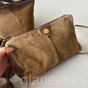 May include: A set of brown textured handbags. The main bag is a rectangular clutch with a gold-colored clasp. The bags have a leather trim and a zipper closure. The bags are in a neutral color palette.