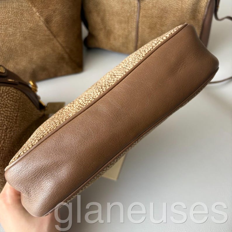 May include: A light brown handbag with a woven texture and brown leather trim. The bag has a rectangular shape with rounded corners. The image shows the side of the bag, highlighting the contrast between the woven material and the smooth leather.