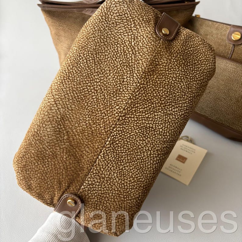 May include: A collection of brown leather handbags with a textured, spotted pattern. The bags have brown leather trim and gold-colored hardware. One bag is in the foreground, with others visible in the background.