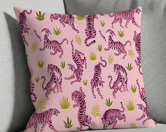 May include: Pink decorative throw pillow with a repeating pattern of pink tigers with dark purple stripes and green foliage on a light pink background. The pillow is square and rests on a gray sofa.