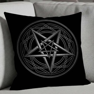 Può includere: Cuscino quadrato nero con un disegno di pentagramma argentato all'interno di un cerchio. Il pentagramma è una stella a cinque punte con una stella più piccola all'interno, su sfondo nero. Il cuscino è su un divano grigio.