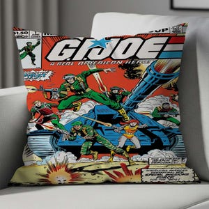 Puede incluir: Un cojín decorativo con un diseño de portada de cómic. La obra de arte presenta el título "G.I. Joe" y escenas de acción con soldados, tanques y explosiones. La paleta de colores incluye rojo, azul, verde y amarillo.