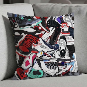 May include: Square throw pillow featuring a collage of colorful sneakers in various styles. The sneakers are in shades of red, black, white, blue, and green. The pillow has a gray border and is placed on a gray sofa.