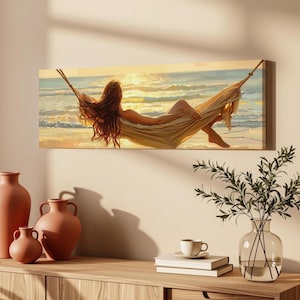 Op de afbeelding: Een rechthoekige canvas print met een persoon met lang haar die rust in een hangmat boven een strand bij zonsondergang. De scène toont gouden licht dat reflecteert op de oceaangolven en het zand, waarbij de persoon naar de horizon kijkt.