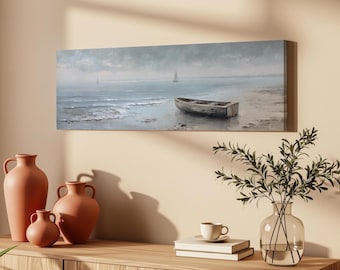 May include: A rectangular canvas wall art print featuring a seascape painting of a wooden rowboat resting on a sandy shore. The scene includes calm blue-grey water, gentle waves, and a distant sailboat under a soft, overcast, cloudy sky.