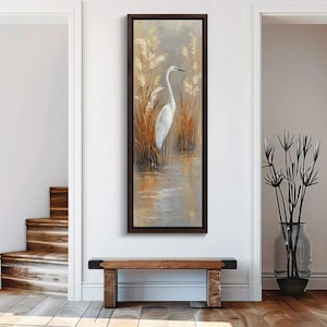 May include: A vertical rectangular wall art piece featuring a painting of a white egret standing in a marsh with tall golden reeds. The artwork is enclosed in a dark brown wooden frame, showcasing a serene nature scene with soft earth tones.