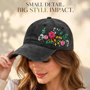 May include: A charcoal gray baseball cap featuring an embroidered floral design on the front panel. The embroidery includes pink, yellow, and white flowers with green leaves. The text SMALL DETAIL. BIG STYLE IMPACT. is printed above the cap.