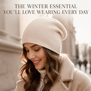 May include: A cream-colored knit beanie hat with a smooth texture. The text above the hat reads: THE WINTER ESSENTIAL YOU'LL LOVE WEARING EVERY DAY. The beanie has a rounded crown and a simple, clean design that fits snugly around the head.