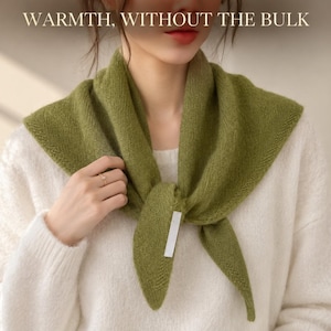 May include: A triangular olive green knit scarf tied around the neck, featuring a fine texture and a small white rectangular tag. The text WARMTH, WITHOUT THE BULK is displayed at the top of the image above the scarf and a white jumper.