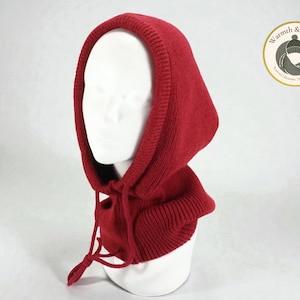 May include: A red knitted hood with a drawstring closure, displayed on a white mannequin head. The hood is a solid color and appears to be made of a soft, warm material. A circular logo with text is visible in the background.