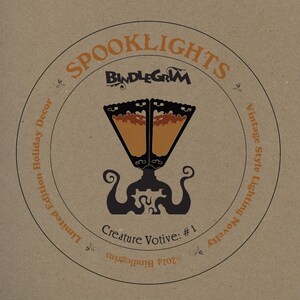 May include: A circular design on a brown background features the text "SPOOKLIGHTS" and "BINDLEGRIM" in orange and black. The design includes a stylized lamp illustration and the words "Creature Votive: #1". The words "Limited Edition Holiday Decor" and "Vintage Style Lighting Novelty" are also present.
