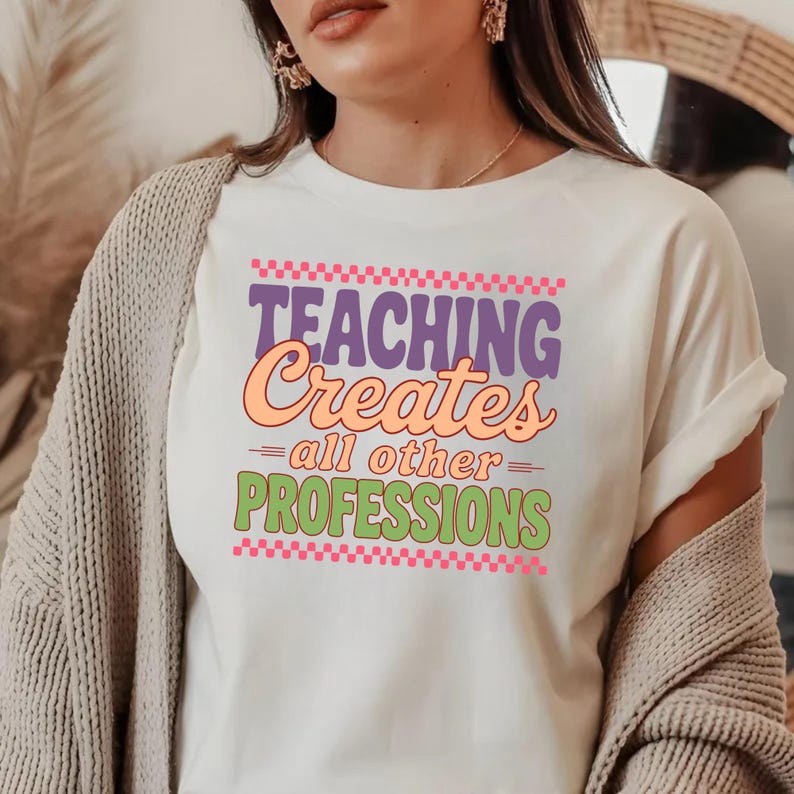 May include: White t-shirt with the text "TEACHING Creates all other PROFESSIONS" in purple, orange, and green. The text is framed by pink and purple checkered patterns. The shirt is a casual wear item.