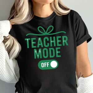 May include: Black t-shirt with the text "TEACHER MODE OFF" in green, featuring a green bow design above the text and an "OFF" switch graphic. The shirt is a casual wear item.