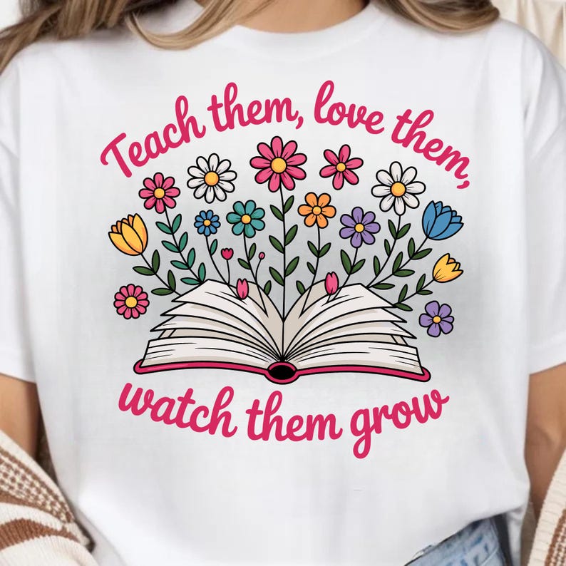 May include: White t-shirt with a colorful floral design and the text "Teach them, love them, watch them grow." The graphic features an open book with flowers in various colors, including pink, yellow, blue, and purple.