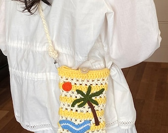 May include: A rectangular crochet crossbody bag featuring a yellow and cream striped pattern. The front displays a small orange sun, a dark green palm tree, and blue wavy lines. It includes a braided cream strap and a single button closure.