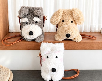 May include: Three plush dog-shaped crossbody bags with fuzzy textures. One is gray and white, one is beige, and one is white with pink accents. Each bag features black button eyes, a black nose, and a thin brown leather-like shoulder strap.