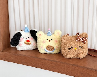May include: Three plush character bags with fuzzy textures. The first is a white dog with black ears and a blue party hat. The second is a yellow bear with a blue party hat. The third is a brown cat with a brown and white polka dot bow.